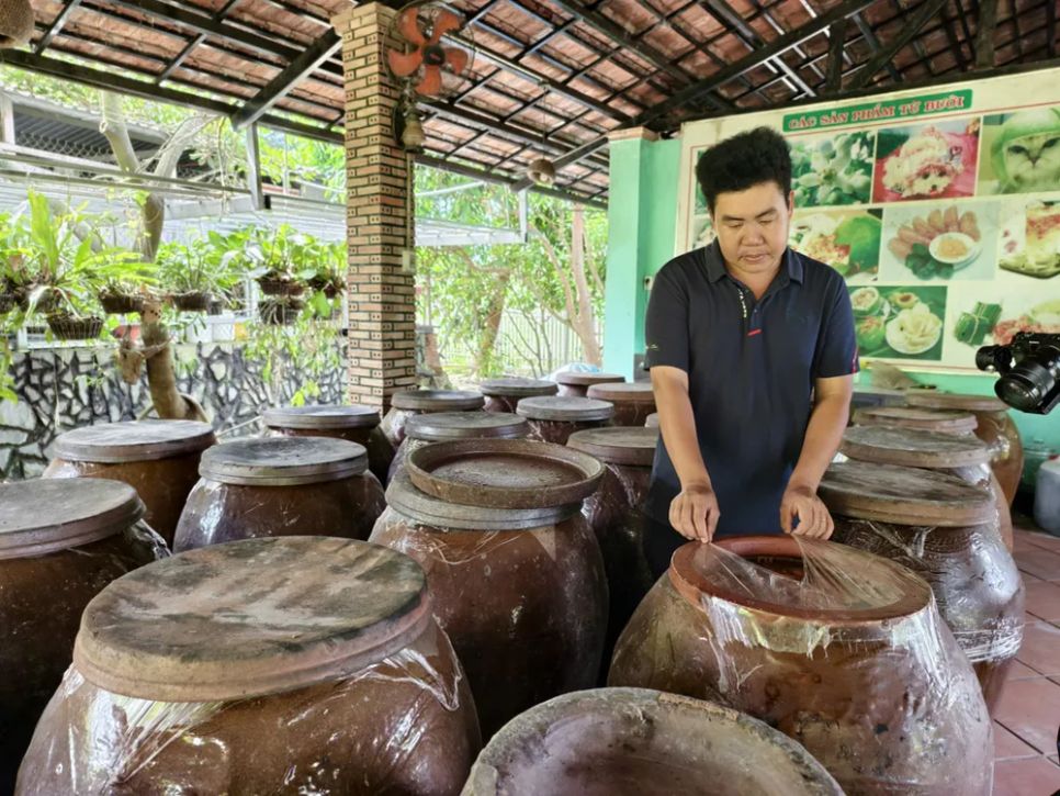 Anh Hồ Hoàng Kha bên sản phẩm nước bưởi lên men đựng trong chum sành