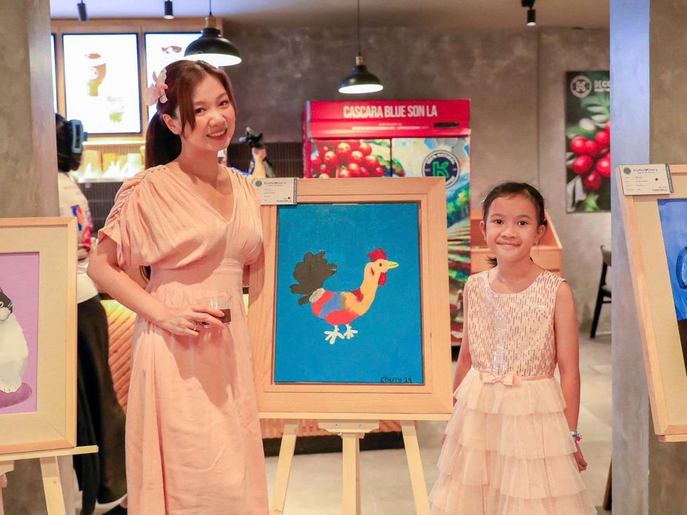 Bé Cherry (tên thật là Phan Ngọc Minh, 9 tuổi, đang sinh sống tại TP.HCM) chụp ảnh cùng khách tham quan triển lãm bên những bức tranh ngộ nghĩnh.