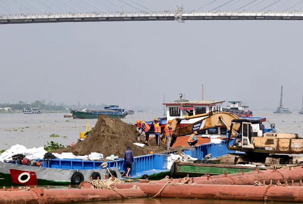 Công nhân được trang bị áo phao thực hiện công đoạn đóng bao tải gia cố mái lòng sông trên sà lan.