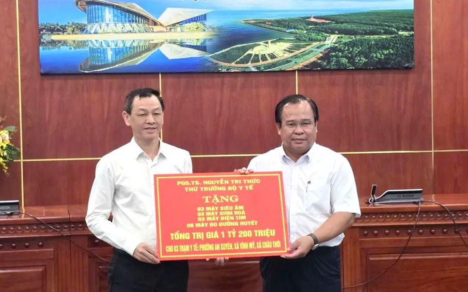 Thứ trưởng Bộ Y tế Nguyễn Tri Thức (bên trái) trao bảng tượng trưng tặng thiết bị y tế cho tỉnh Cà Mau