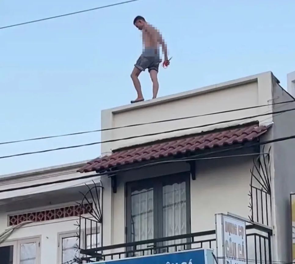 Nam thanh niên cố thủ trên mái nhà. Ảnh: H.T.